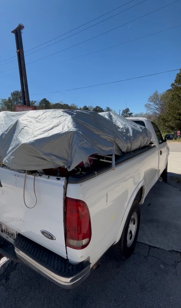 The company's white pickup truck parked with its bed loaded and a silver tarp strapped down over the load, ready to haul away